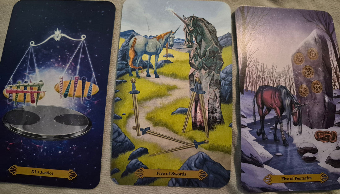 Three tarot cards laid out for a daily collective reading: Justice (XI), Five of Swords, and Five of Pentacles from a unicorn tarot deck