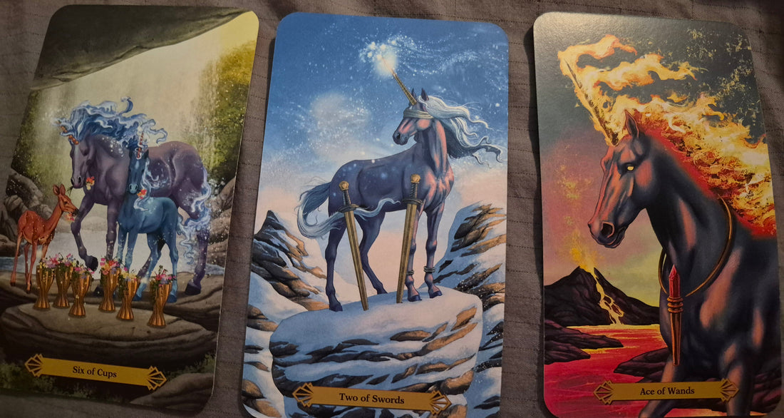 Three tarot cards laid out: Six of Cups, Two of Swords, and Ace of Wands from the unicorn tarot deck