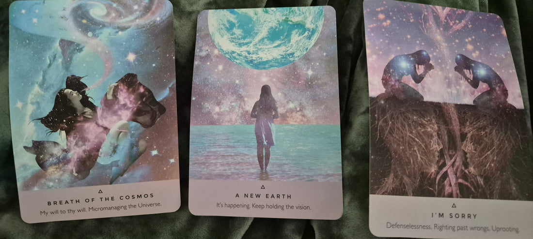 Three oracle cards: Breath of the Cosmos, A New Earth, and I'm Sorry laid on a dark green velvet background