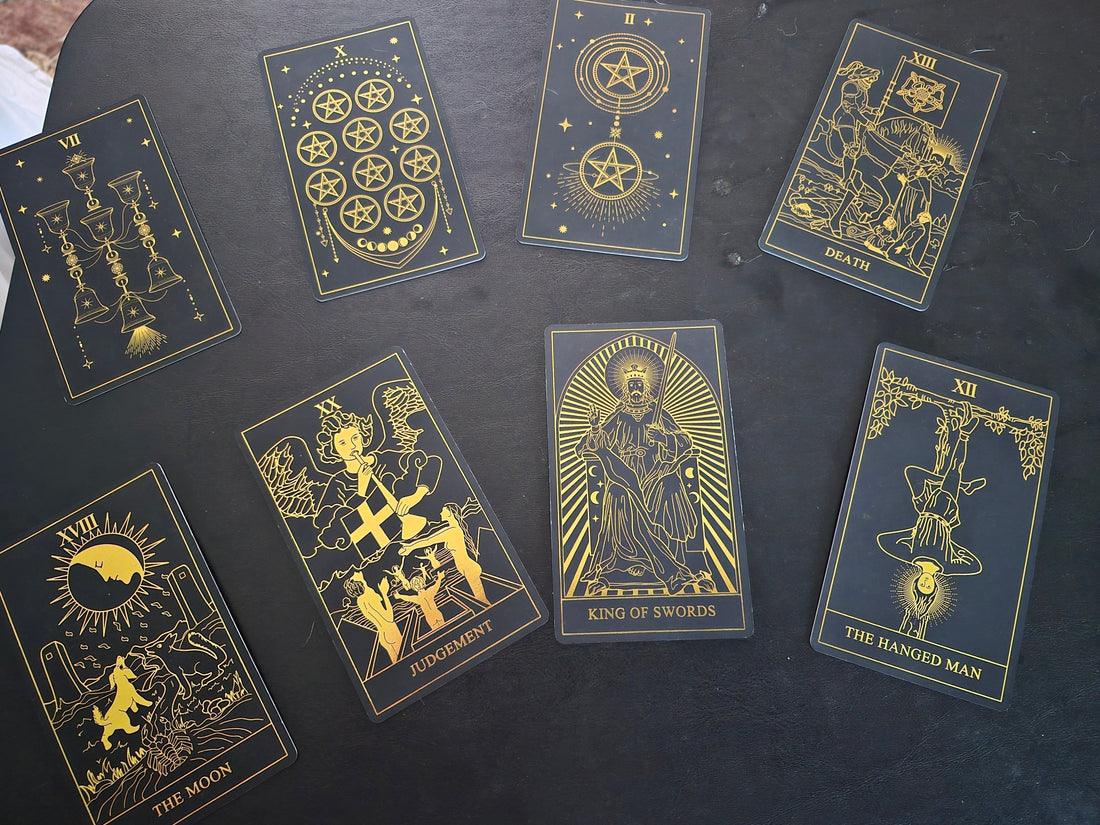 Eight tarot cards spread on a dark table — Seven of Cups, Ten of Pentacles, Two of Pentacles, Death, The Moon, Judgement, King of Swords, and The Hanged Man