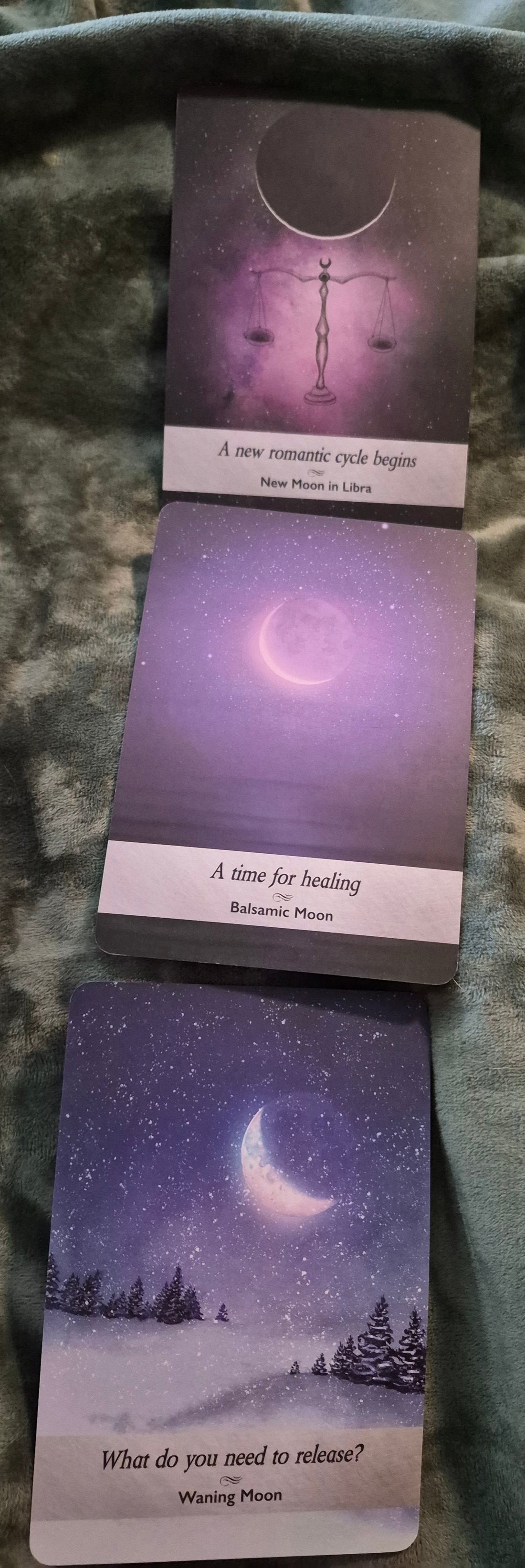 Three lunar oracle cards: New Moon in Libra, Balsamic Moon, and Waning Moon laid on a soft grey blanket