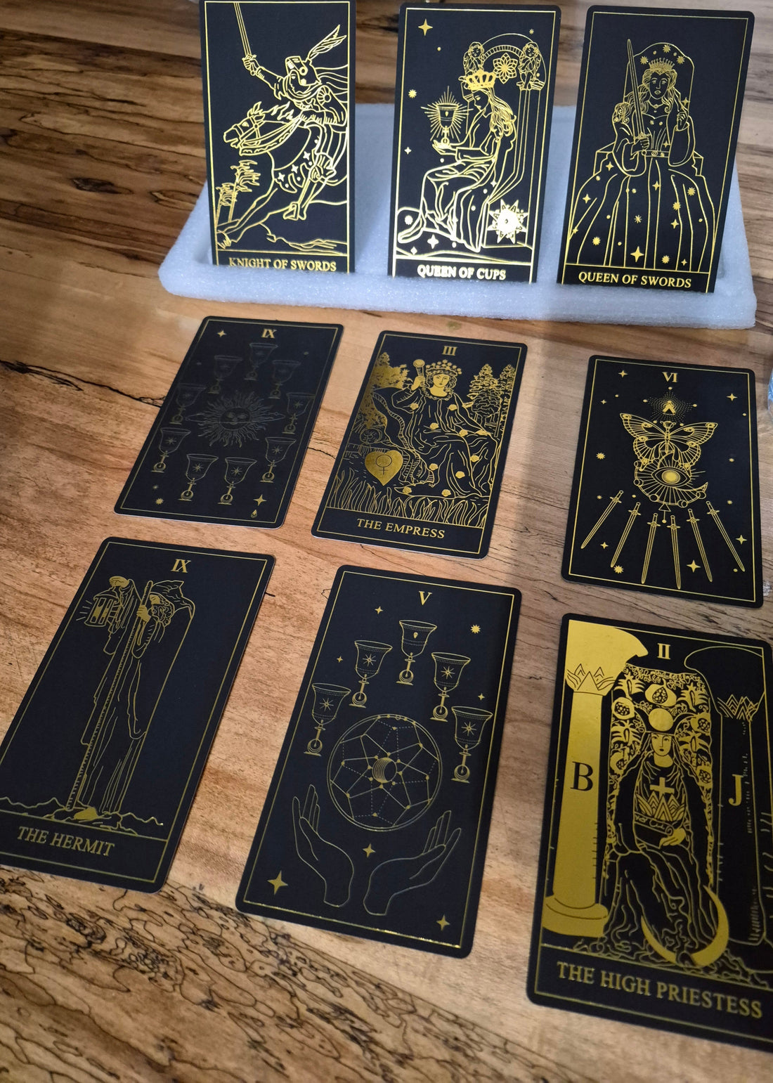Black and gold tarot cards spread on a wooden table including The High Priestess, The Empress, The Hermit, and more