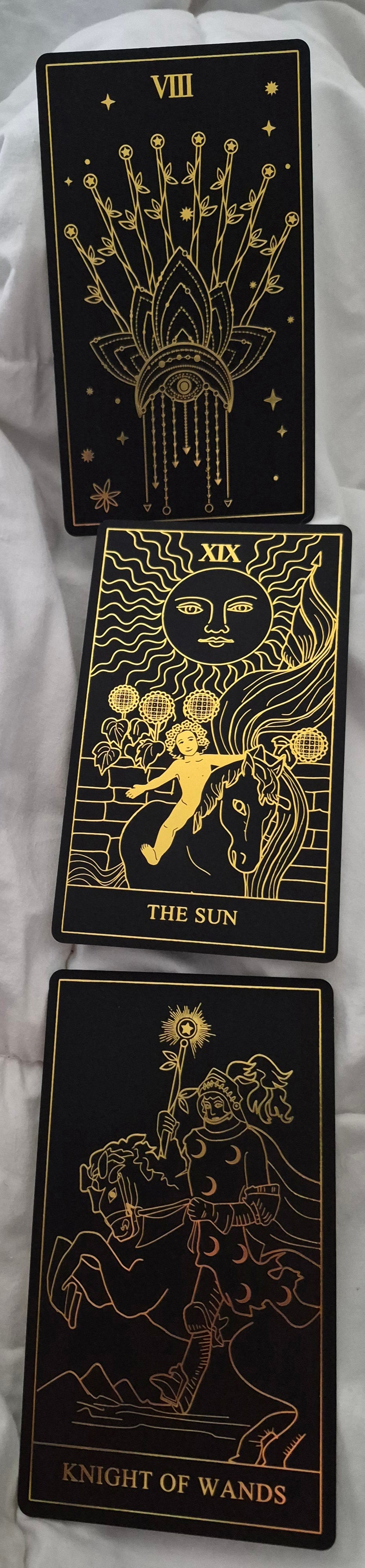 Three tarot cards: Strength VIII, The Sun XIX, and Knight of Wands on a dark luxury background with gold foil details