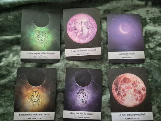 Six moon oracle cards spread on a velvet surface featuring New Moon in Virgo, Full Moon in Libra, Balsamic Moon, New Moon in Leo, New Moon in Aquarius, and Full Moon in Aries