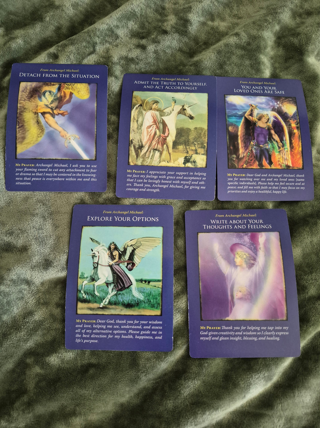 Five Archangel Michael oracle cards spread on a green velvet surface