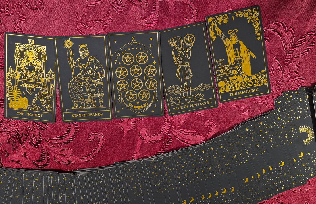 Five tarot cards laid out on red velvet fabric: The Chariot, King of Wands, Ten of Pentacles, Page of Pentacles, and The Magician — black and gold luxury tarot deck