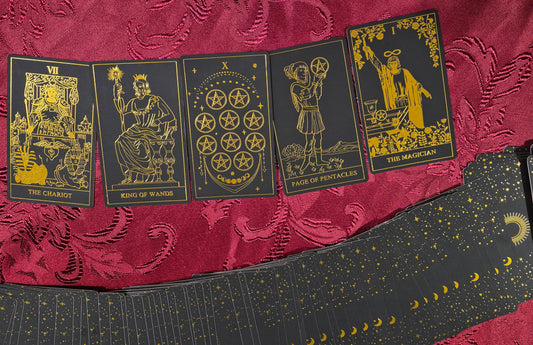 Five tarot cards laid out on red velvet fabric: The Chariot, King of Wands, Ten of Pentacles, Page of Pentacles, and The Magician — black and gold luxury tarot deck