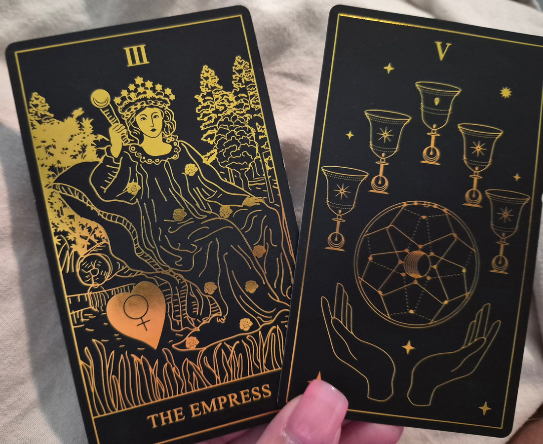Daily collective tarot reading cards – The Empress and Five of Cups from a black and gold tarot deck