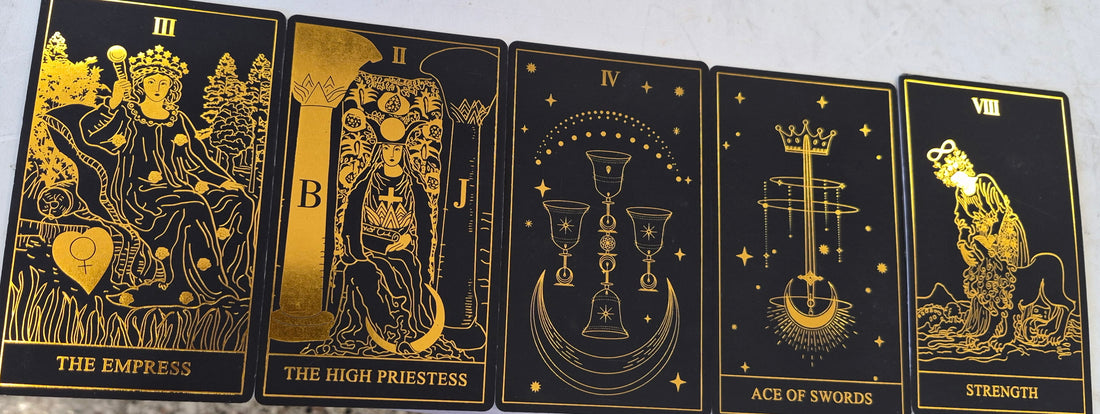 Five gold-on-black tarot cards: The Empress, The High Priestess, Four of Cups, Ace of Swords, and Strength.